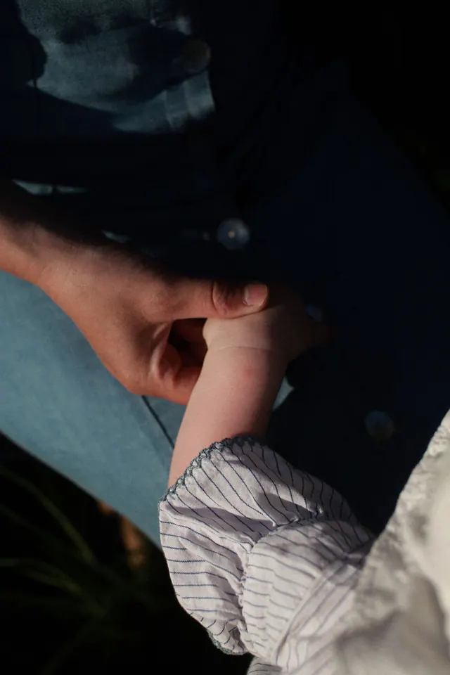 يد طفل ممسوكة بيد أحد والديه، صورة توضيحية للأسرة والرعاية